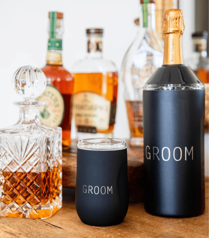Black 'GROOM' wine cooler and tumblers with bottles in the background